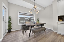 Spacious dining area featuring wood-finish flooring, a contemporary chandelier, large window with natural light, a white exterior door, and built-in cabinetry with a dark tile backsplash - 