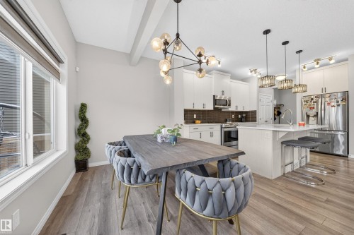 Open-concept kitchen and dining area featuring light wood-finish flooring, a contemporary chandelier, white cabinetry, stainless steel appliances, and an island with bar seating - 6085 King Landing, Edmonton, AB - Indoor