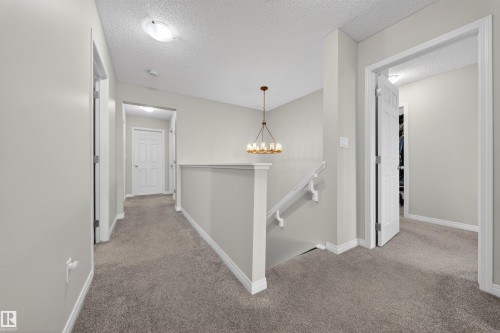 Upper-level landing featuring a bronze-finish chandelier, neutral carpet flooring, and white trim - 6085 King Landing, Edmonton, AB - Indoor Photo Showing Other Room