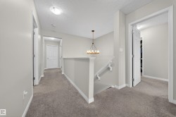Upper-level landing featuring a bronze-finish chandelier, neutral carpet flooring, and white trim - 