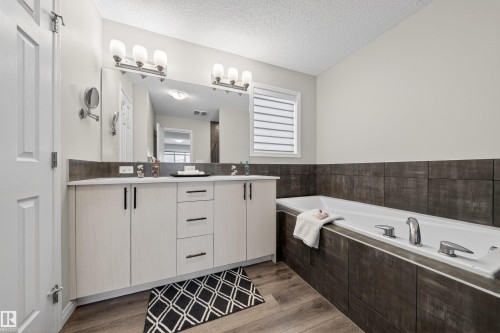 Spacious bathroom featuring a built-in bathtub, a double vanity with light wood-finish cabinetry, a large mirror, and wood-finish flooring - 6085 King Landing, Edmonton, AB - Indoor Photo Showing Bathroom