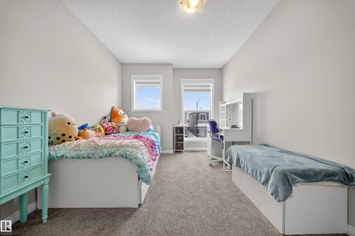 Light grey wall paint with textured ceiling, two windows, carpet flooring, and a built-in desk with shelving - 6085 King Landing, Edmonton, AB - Indoor Photo Showing Bedroom