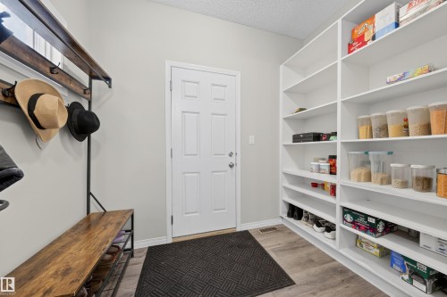 Dedicated pantry area featuring extensive built-in shelving, durable wood-finish flooring, a six-panel door, and a built-in coat rack with bench seating - 6085 King Landing, Edmonton, AB - Indoor With Storage