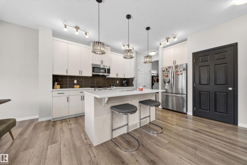 Kitchen featuring light-toned cabinetry, stainless steel appliances, a center island with seating, dark subway tile backsplash, and wood-finish flooring - 6085 King Landing, Edmonton, AB - Indoor Photo Showing Kitchen With Upgraded Kitchen