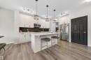Kitchen featuring light-toned cabinetry, stainless steel appliances, a center island with seating, dark subway tile backsplash, and wood-finish flooring - 6085 King Landing, Edmonton, AB  - Indoor Photo Showing Kitchen With Upgraded Kitchen 