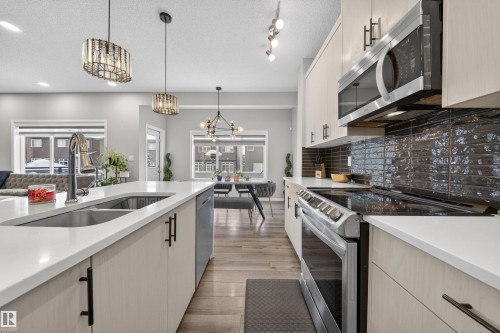 Contemporary kitchen featuring a large island with an undermount sink, light-toned cabinetry with matte black hardware, stainless steel appliances, dark subway tile backsplash, and wood-finish flooring - 6085 King Landing, Edmonton, AB - Indoor Photo Showing Kitchen With Double Sink With Upgraded Kitchen