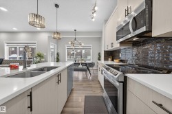 Contemporary kitchen featuring a large island with an undermount sink, light-toned cabinetry with matte black hardware, stainless steel appliances, dark subway tile backsplash, and wood-finish flooring - 