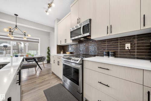 Modern kitchen featuring light-toned cabinetry, stainless steel appliances, a dark tile backsplash, white countertops, and wood-finish flooring - 6085 King Landing, Edmonton, AB - Indoor Photo Showing Kitchen With Upgraded Kitchen