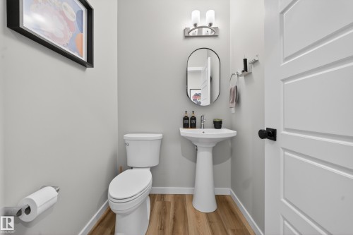 Pedestal sink with a modern oval mirror, sleek wall-mounted lighting fixture, and wood-finish flooring - 3337 Kulay Way, Edmonton, AB - Indoor Photo Showing Bathroom