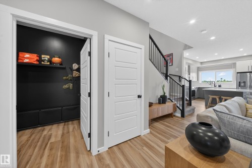 Open living area featuring wood-finish flooring, a built-in closet with shelving, a staircase with black metal railings, recessed lighting, and a modern kitchen with a large window - 3337 Kulay Way, Edmonton, AB - Indoor