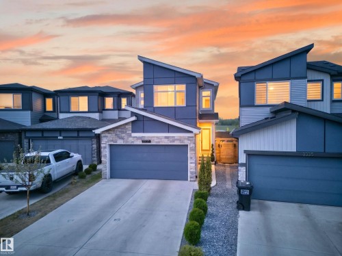 Contemporary exterior featuring a distinctive sloped roofline, mixed material siding, stone accents, a two-car garage, and a concrete driveway - 3337 Kulay Way, Edmonton, AB - Outdoor With Facade