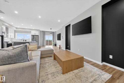 Open-concept living area featuring wood-finish flooring, recessed lighting, a modern kitchen with white cabinetry, and a sliding glass door leading to an outdoor space - 3337 Kulay Way, Edmonton, AB - Indoor Photo Showing Living Room