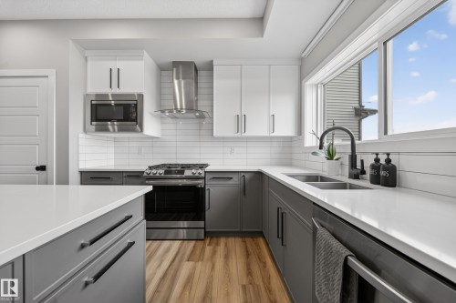 Modern kitchen featuring two-tone cabinetry, stainless steel appliances, wood-finish flooring, white countertops, and a subway tile backsplash - 3337 Kulay Way, Edmonton, AB - Indoor Photo Showing Kitchen With Double Sink With Upgraded Kitchen