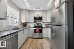 Kitchen featuring light wood-finish flooring, white cabinetry, dark countertops, and a white subway tile backsplash - 