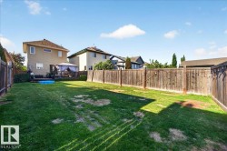 Expansive fenced backyard featuring a substantial lawn area, a back deck, and mature privacy hedging - 