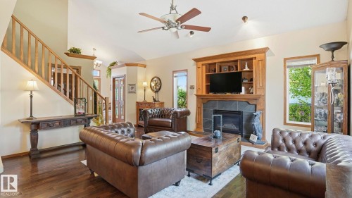 Spacious living area featuring vaulted ceilings, wood-finish flooring, a built-in entertainment center with shelving, a fireplace with a stone surround, and an open staircase with wood railings - 4309 37A Avenue, Edmonton, AB - Indoor Photo Showing Living Room With Fireplace