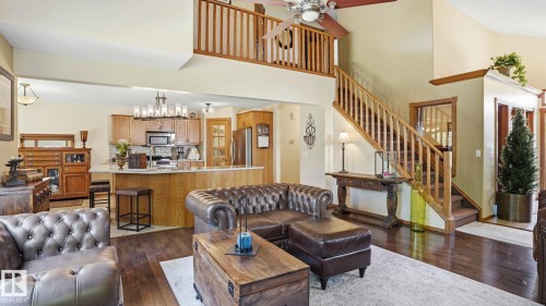 Open-concept living space featuring wood-finish flooring, a two-story ceiling, a staircase with wood railing, a kitchen island with seating, and wood cabinetry - 4309 37A Avenue, Edmonton, AB - Indoor Photo Showing Living Room