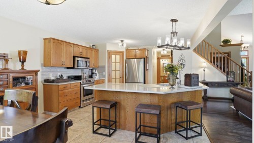 Spacious kitchen featuring an angled island with seating, stainless steel appliances, wood cabinetry, tile flooring, and a subway tile backsplash - 4309 37A Avenue, Edmonton, AB - Indoor Photo Showing Kitchen