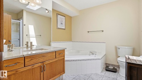 Bathroom featuring a corner jetted tub with tile surround, a double vanity with stone countertop and integrated sinks, a separate toilet, and tiled flooring - 4309 37A Avenue, Edmonton, AB - Indoor Photo Showing Bathroom