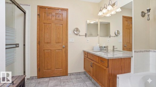Bathroom featuring a dual-sink vanity with a light-toned countertop, wood-finish cabinetry, and a large wall mirror - 4309 37A Avenue, Edmonton, AB - Indoor Photo Showing Bathroom