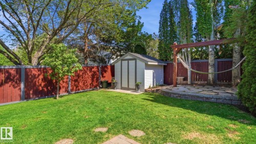 Fenced backyard featuring a manicured lawn, stone patio, storage shed, and a wooden pergola structure - 4309 37A Avenue, Edmonton, AB - Outdoor
