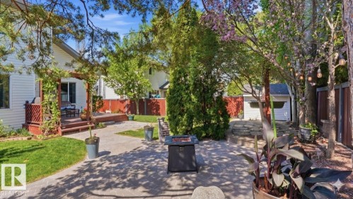 Paver patio featuring a fire pit, bordered by a wooden deck with a pergola, and surrounded by mature trees and shrubs - 4309 37A Avenue, Edmonton, AB - Outdoor