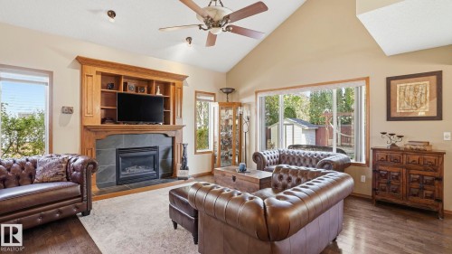 Living area featuring vaulted ceilings, a built-in entertainment center with shelving, a fireplace with a stone surround, and wood-finish flooring - 4309 37A Avenue, Edmonton, AB - Indoor Photo Showing Living Room With Fireplace