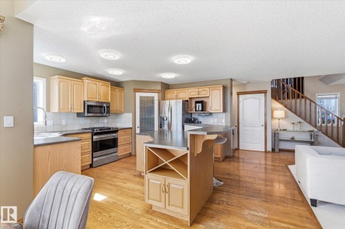 Kitchen featuring natural wood cabinetry, stainless steel appliances, a tile backsplash, and an island with a built-in wine rack - 442 Hunters Green, Edmonton, AB - Indoor Photo Showing Kitchen
