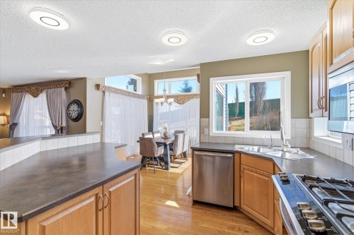 Kitchen featuring wood-finish cabinetry, stainless steel appliances, dark countertops, and a tile backsplash - 442 Hunters Green, Edmonton, AB - Indoor Photo Showing Kitchen