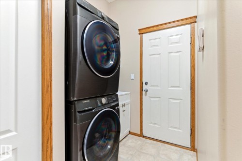 Dedicated laundry space featuring a stacked washer and dryer, tile flooring, and a white paneled door with wood trim - 442 Hunters Green, Edmonton, AB - Indoor Photo Showing Laundry Room