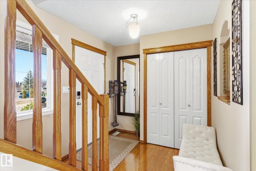 Entry foyer featuring polished wood-finish flooring, a wood baluster staircase, a white paneled entry door, and a flush-mount ceiling light fixture - 442 Hunters Green, Edmonton, AB - Indoor Photo Showing Other Room