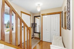 Entry foyer featuring polished wood-finish flooring, a wood baluster staircase, a white paneled entry door, and a flush-mount ceiling light fixture - 