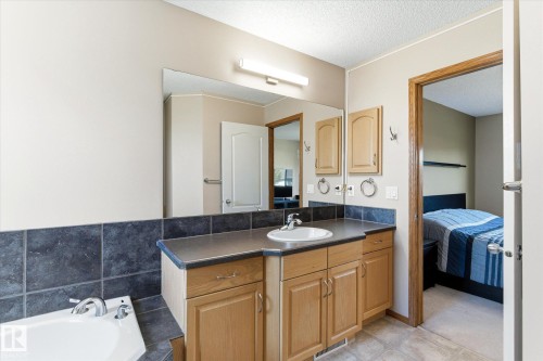 Bathroom vanity featuring a single basin sink set in a dark countertop, light wood-finish cabinetry, and a large wall-mounted mirror - 442 Hunters Green, Edmonton, AB - Indoor Photo Showing Bathroom