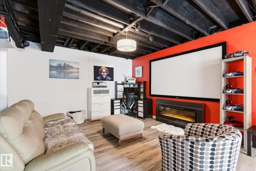 Entertainment space featuring a large projection screen, built-in electric fireplace, and wood-finish flooring - 442 Hunters Green, Edmonton, AB - Indoor With Fireplace