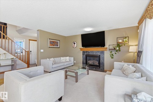 Living area featuring a tiled fireplace with a wood mantel, a built-in television mount, and light neutral carpeting - 442 Hunters Green, Edmonton, AB - Indoor Photo Showing Living Room With Fireplace