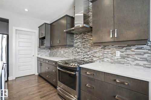 Contemporary kitchen featuring dark wood-finish cabinetry, light-toned countertops, a mosaic tile backsplash, stainless steel appliances, and recessed lighting - 1915 77 Street, Edmonton, AB - Indoor Photo Showing Kitchen With Upgraded Kitchen