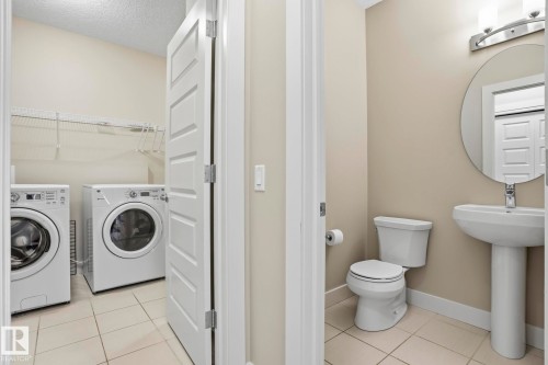 Pedestal sink with a circular mirror, toilet, and tile flooring - 1915 77 Street, Edmonton, AB - Indoor Photo Showing Laundry Room