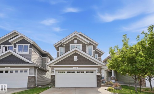 Modern architectural facade featuring gabled rooflines, dark shake siding accents, light horizontal siding, stone veneer details, and a two-car garage with transom windows - 1915 77 Street, Edmonton, AB - Outdoor With Facade