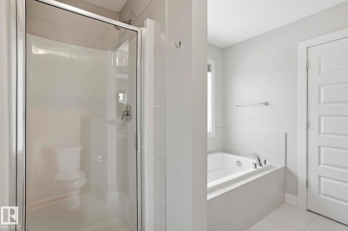 Spacious bathroom featuring a glass-enclosed shower, a separate built-in bathtub with tile surround, a window for natural illumination, and light-toned tile flooring - 1915 77 Street, Edmonton, AB - Indoor Photo Showing Bathroom