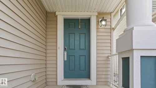 Front entrance featuring a paneled door, exterior wall lantern, and column with railing - 1915 77 Street, Edmonton, AB - Outdoor With Exterior