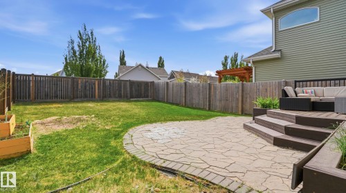 Expansive backyard featuring a stone patio with a rounded edge, tiered composite decking, wood fencing, and raised garden beds - 1915 77 Street, Edmonton, AB - Outdoor