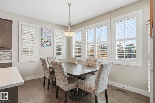 Dining area featuring wood-finish flooring, a contemporary chandelier, and multiple windows with plantation shutters - 1915 77 Street, Edmonton, AB - Indoor Photo Showing Dining Room