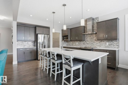 Modern kitchen featuring a large central island with a white countertop, dark wood-finish cabinetry, stainless steel appliances, a tile backsplash, and dark wood-finish flooring - 1915 77 Street, Edmonton, AB - Indoor Photo Showing Kitchen With Stainless Steel Kitchen With Upgraded Kitchen