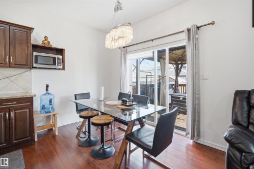 Dining area with wood-finish flooring featuring a contemporary chandelier, sliding glass door, and rich wood cabinetry with a light-colored backsplash - 1523 36 Avenue, Edmonton, AB - Indoor Photo Showing Dining Room