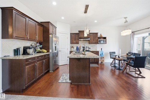 Open-concept kitchen featuring dark wood cabinetry, light granite countertops, stainless steel appliances, and wood-finish flooring - 1523 36 Avenue, Edmonton, AB - Indoor Photo Showing Kitchen