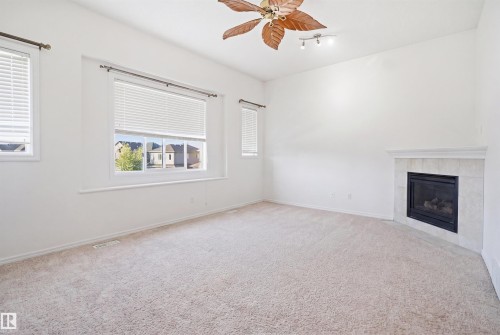 Room featuring a corner fireplace with a tiled surround, neutral carpeting, multiple windows with blinds, a ceiling fan, and track lighting - 1523 36 Avenue, Edmonton, AB - Indoor With Fireplace