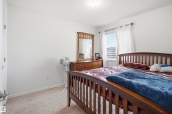 Bedroom featuring neutral carpeting, white walls, and a window with horizontal blinds and sheer curtains - 