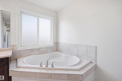 Corner soaking tub with polished chrome fixtures, surrounded by tiled decking and a tiled wainscoting - 1523 36 Avenue, Edmonton, AB - Indoor Photo Showing Bathroom