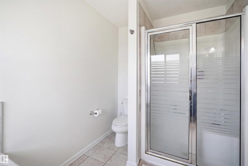 Bathroom featuring a sliding glass shower enclosure with frosted privacy bands, a white toilet, and tiled flooring - 1523 36 Avenue, Edmonton, AB - Indoor Photo Showing Bathroom