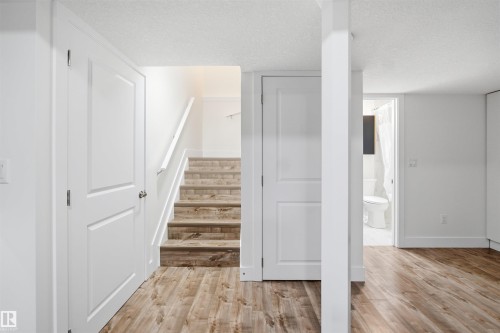 Spacious lower level featuring wood-finish flooring, white panel doors, a staircase with wood-finish treads, and a bathroom with a white toilet and shower curtain - 1523 36 Avenue, Edmonton, AB - Indoor Photo Showing Other Room